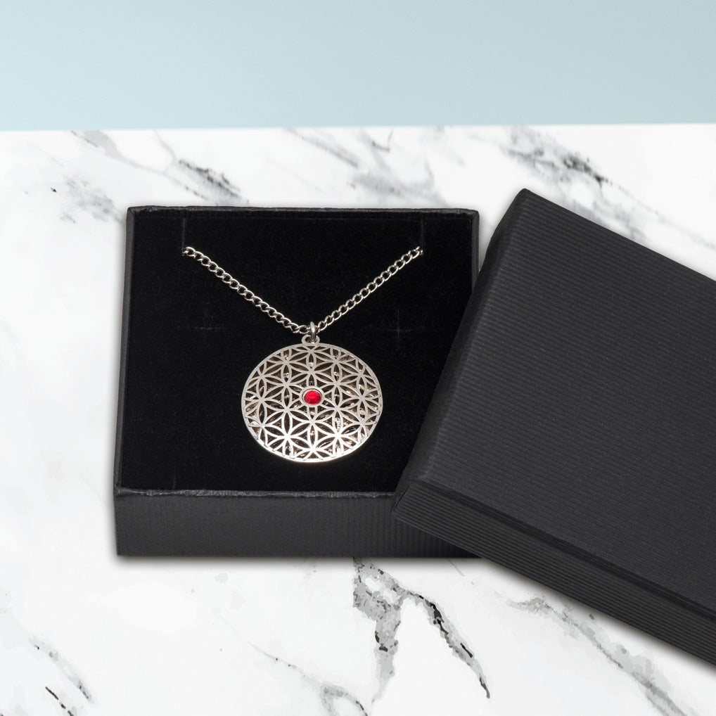 Der Anhänger Blume des Lebens mit rotem Stein wird mit einer Gliederkette in einem Schmuckkästchen